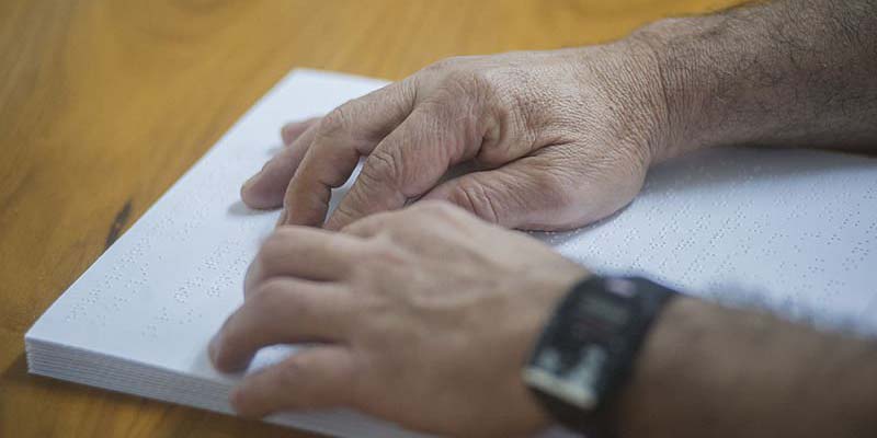 Close das mãos de um homem tateando um livro em braille.