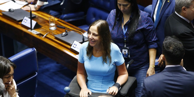 Foto tirada de cima de Mara no plenário do Senado. Entre alguns parlamentares ela sorri.
