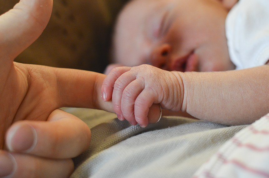 Foto de um bebê segurando o dedo indicador de sua mãe.