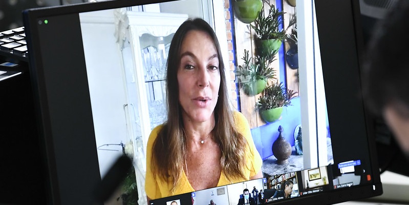 A imagem de Mara é transmitida em uma tela de computador. Ela discursa.