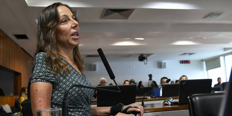 Foto de perfil da Senadora Mara Gabrilli a frente de um microfone de mesa de uma comissão do Senado.