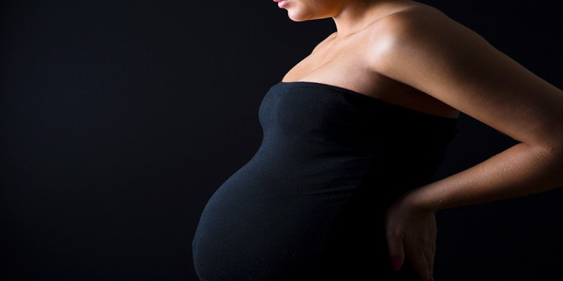 Foto de uma grávida, usando um vestido preto, a imagem também possui um fundo preto.